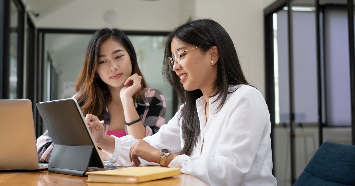  two female college students working on digital tablet and talking about lessons