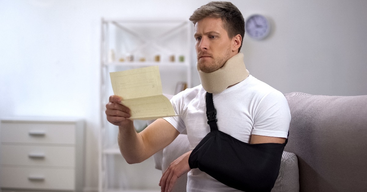 Man in foam cervical collar and arm sling reading medical bill