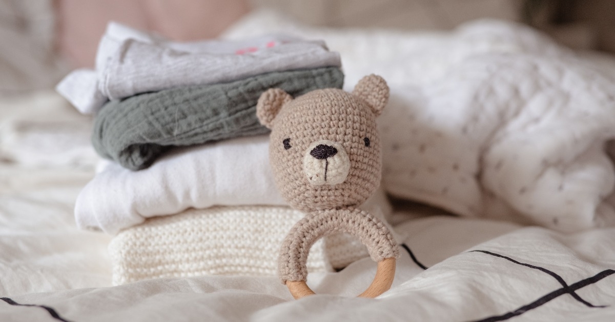baby clothes with diapers are stacked with a pacifier and a toy bear