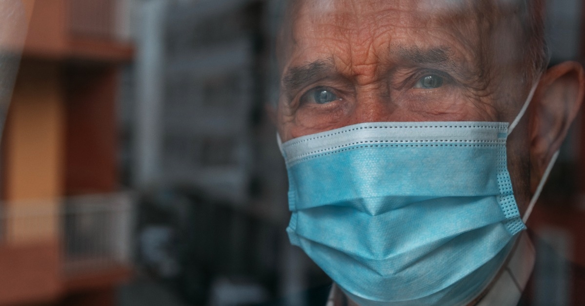 elderly man with face mask looking out the window