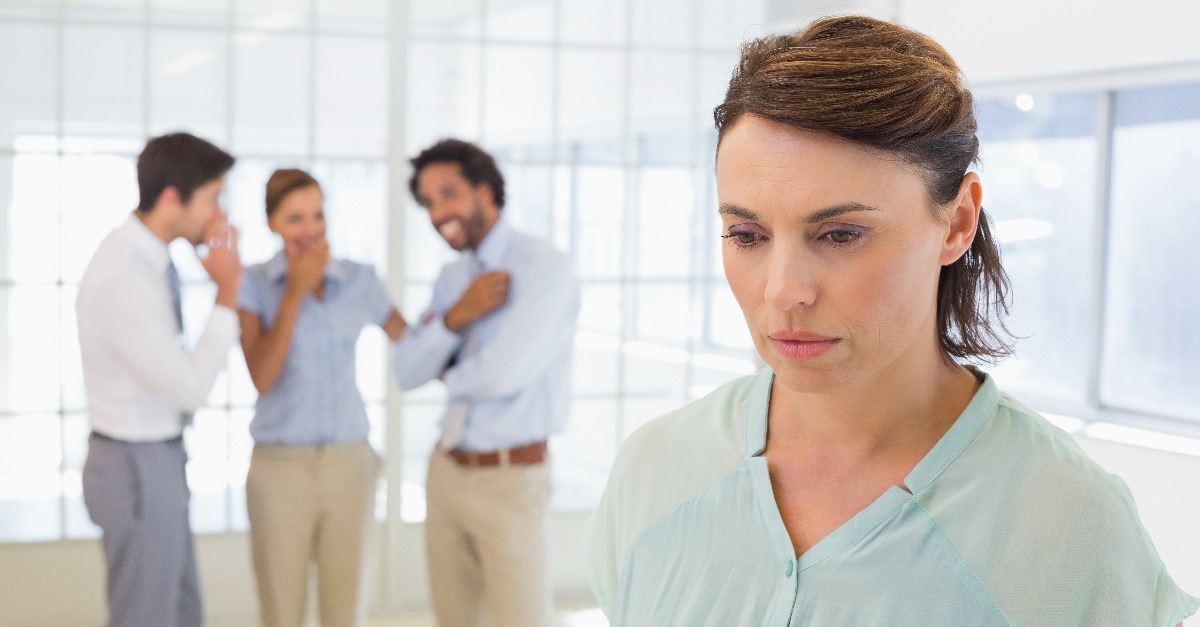 Colleauges gossiping with sad businesswoman in foreground