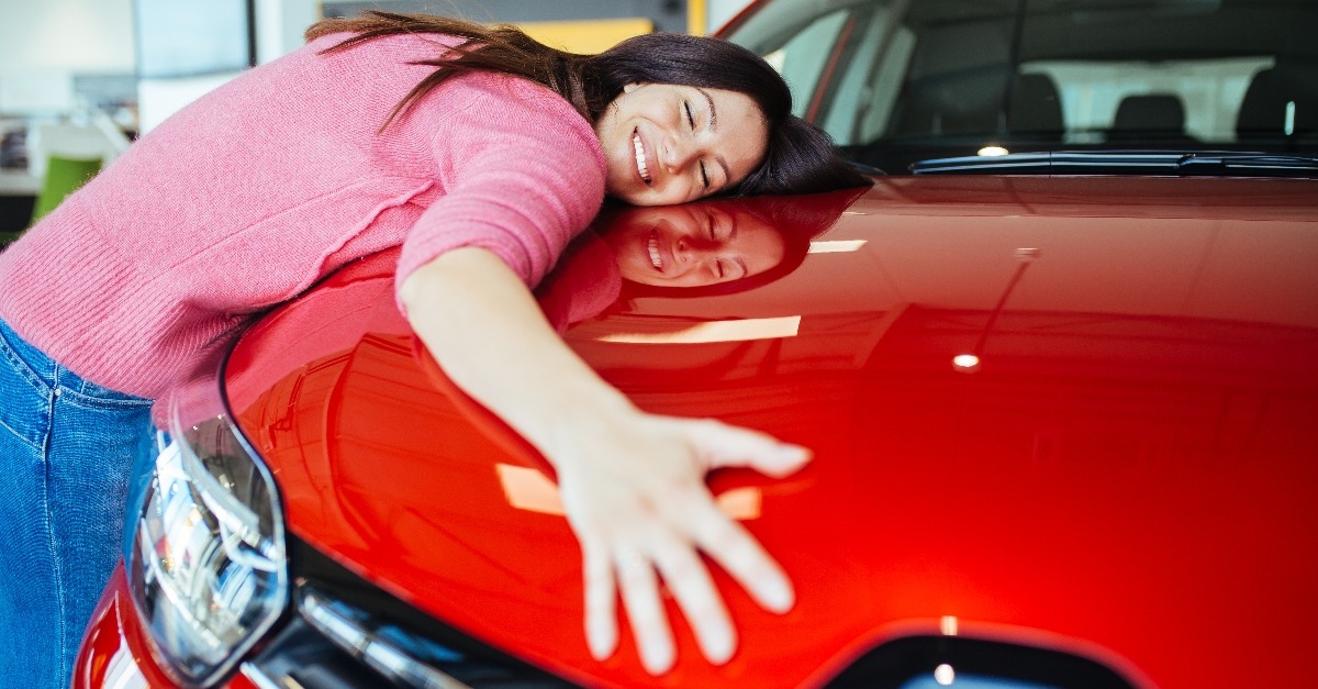Happy beautiful young woman buying a new car at the car showroom
