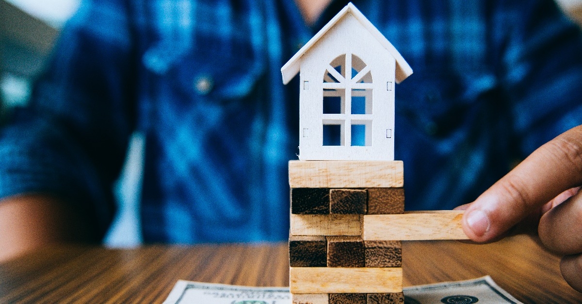 Hand holding a piece of wood block with model white house on dollar banknote