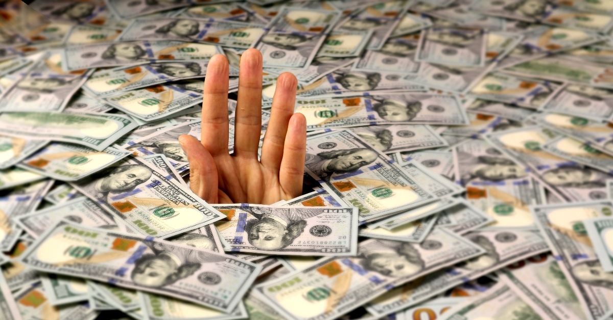 hand sticks out of a mountain of dollars