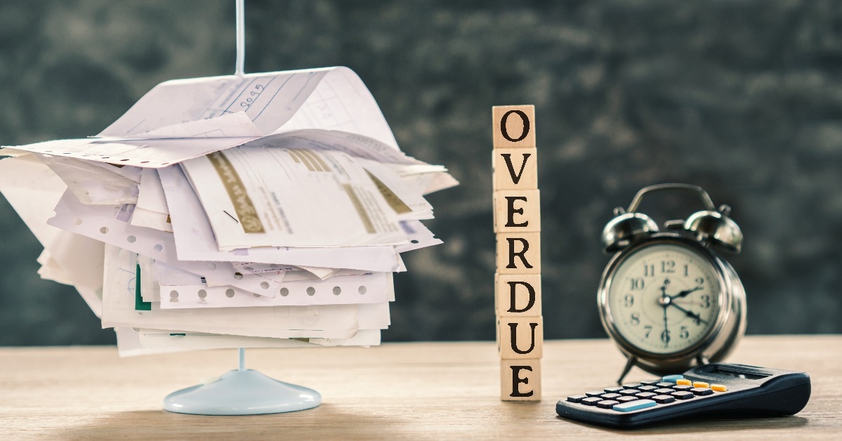 overdue concept with stack of unpaid bills calculator and clock on table