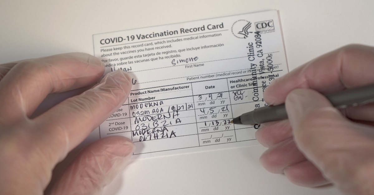 gloved hands adding booster dose to a Covid 19 vaccination card