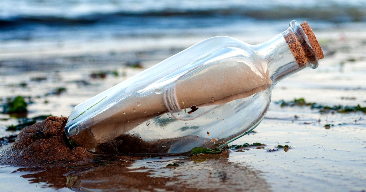 message in a glass bottle with a cork washing away on sandy beach