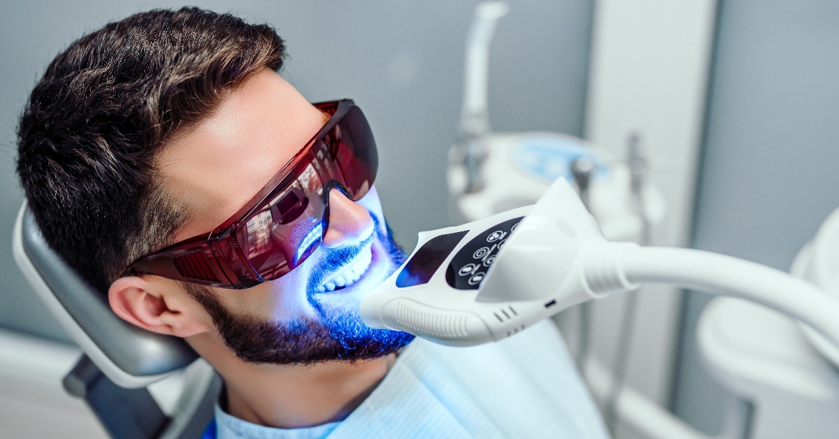 dentist starting teeth whitening procedure with young man