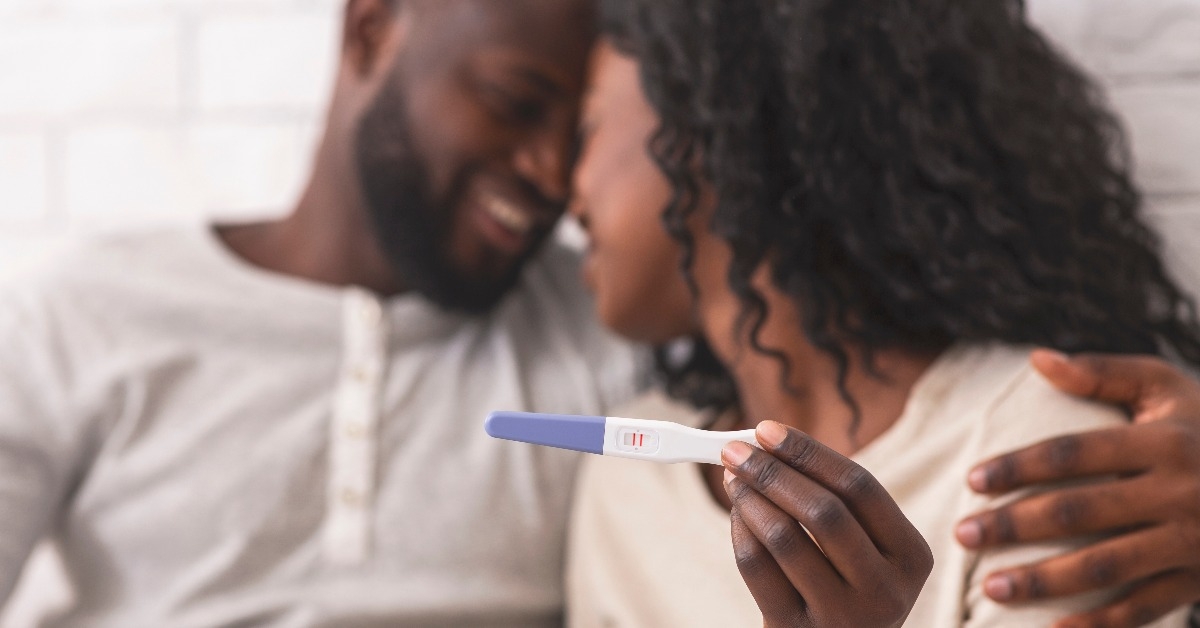 happy afro couple holding pregnancy test with positive result
