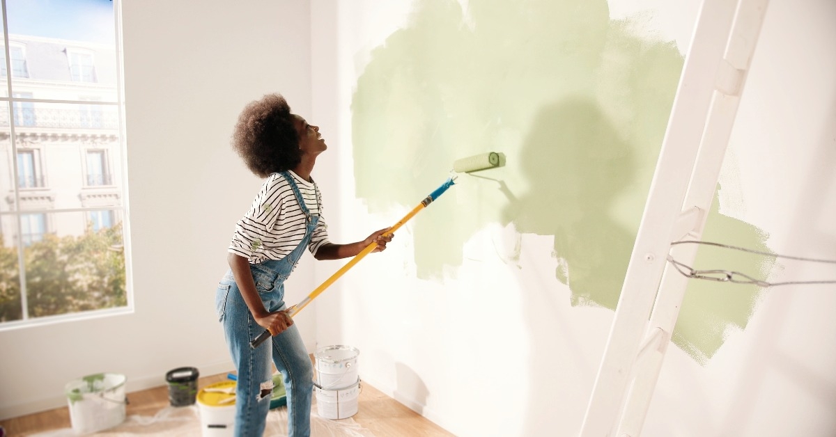 woman dancing and painting wall with roller brush 