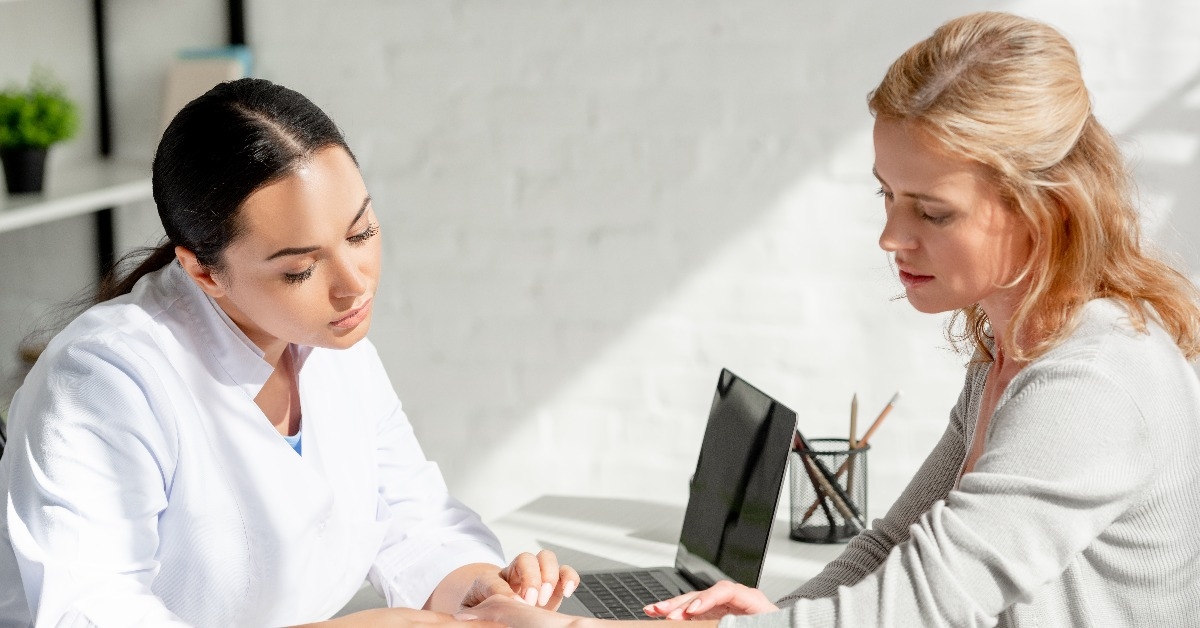 dermatologist sitting at table examining skin of patient in clinic