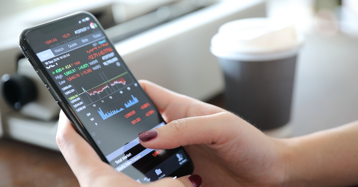 female hand with smartphone trading stock online in coffee shop