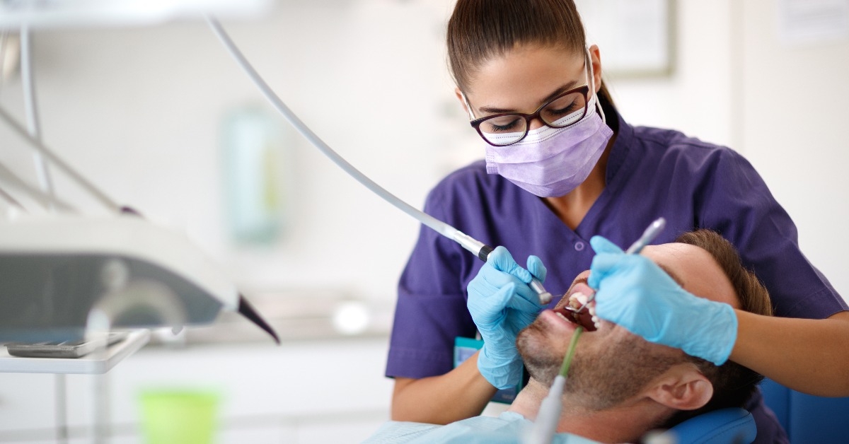 young female dentist drilling tooth to patient