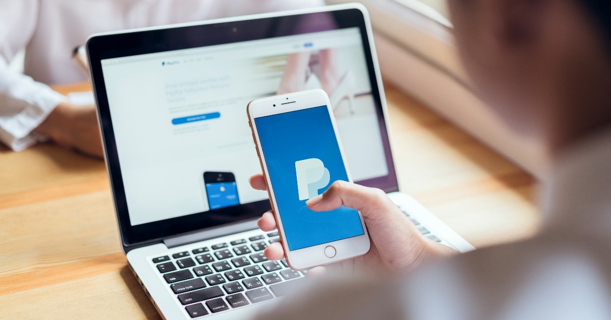 woman uses smartphone on the table  showing screen Paypal web page