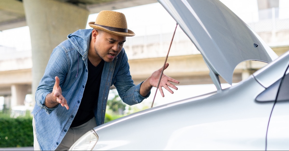 asian man looking at broken down car engine on street 