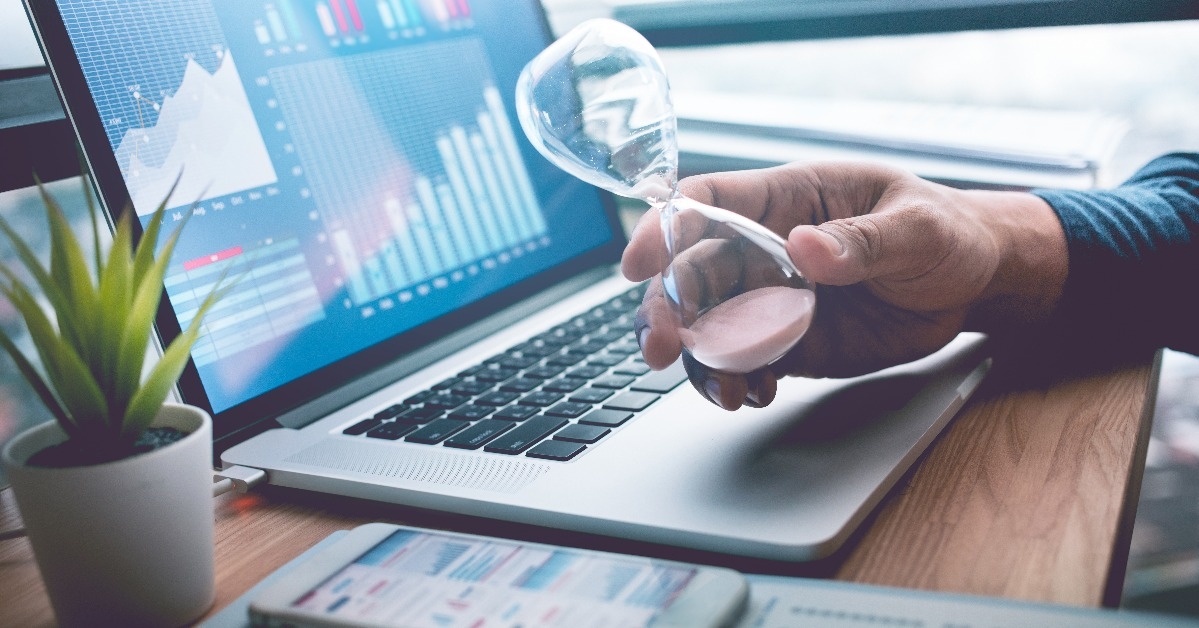 businessman holding hourglass with graph chart on laptop