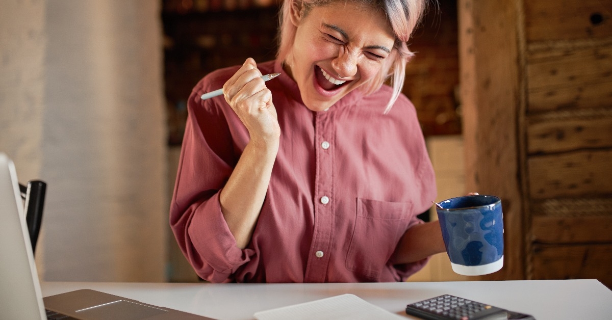 cheerful young female sitting at desk with calculator and laptop