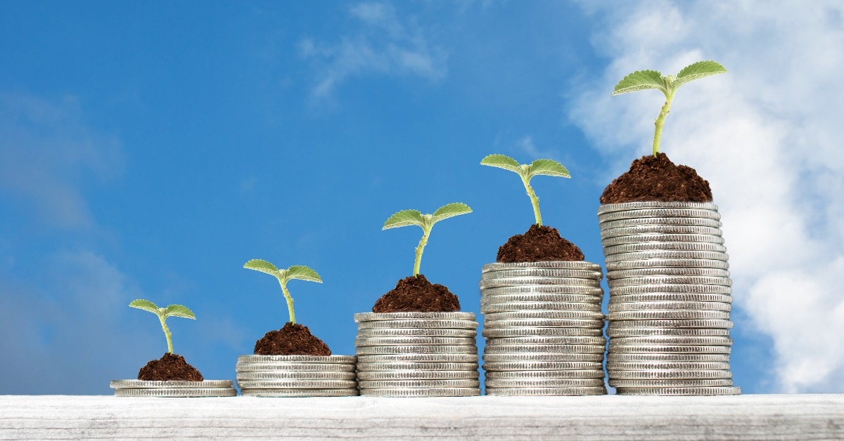 stacks of coins with growing plants against blue sky