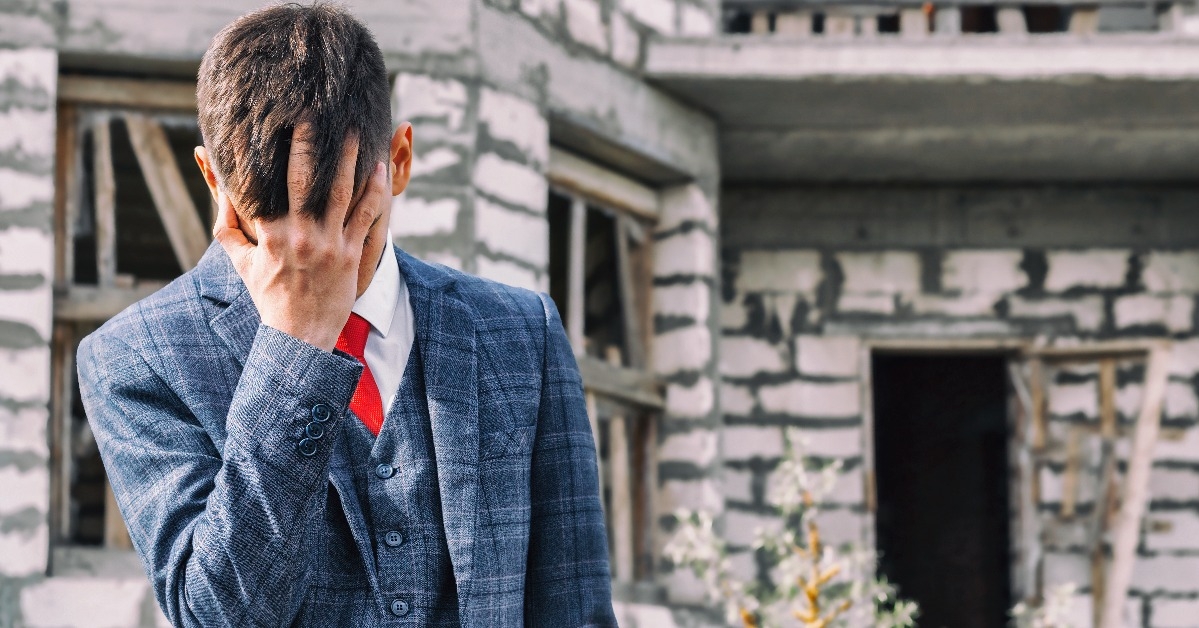 young man in fashionable suit stands on the background of destroyed unfinished house