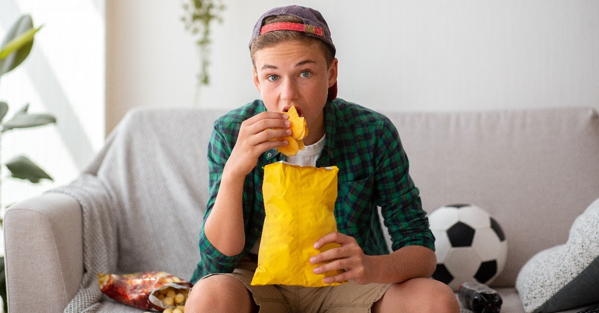 teenager watching football game and eating unhealthy food