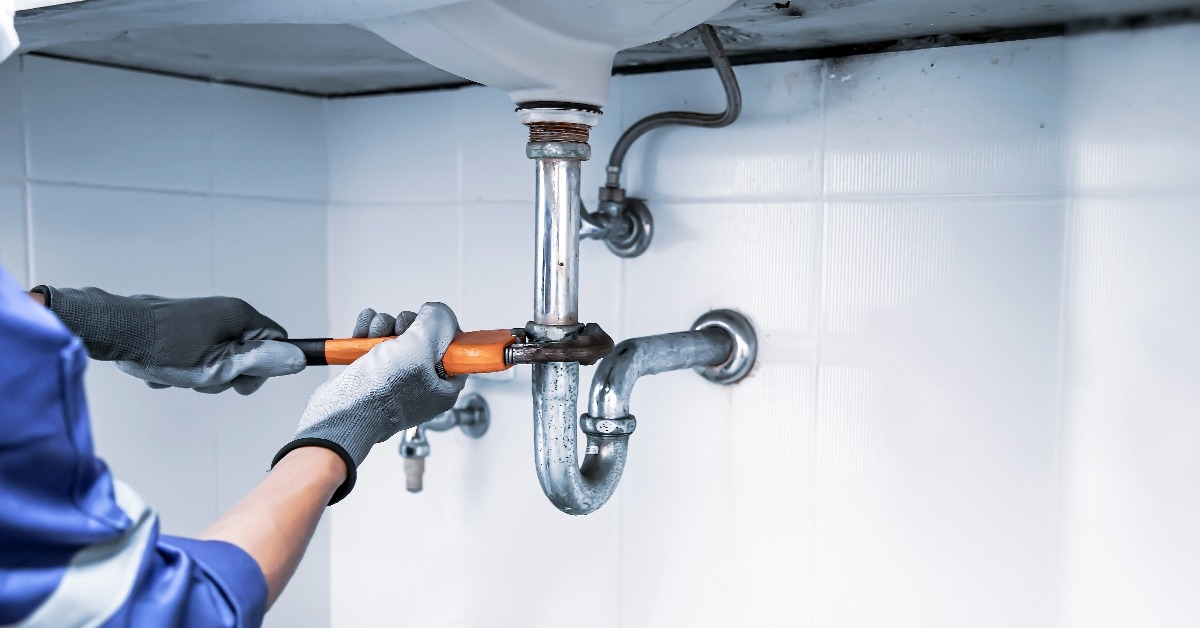 plumber using a wrench to repair a water pipe under the sink