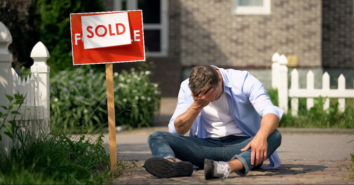 extremely depressed man sitting on ground by sold signboard