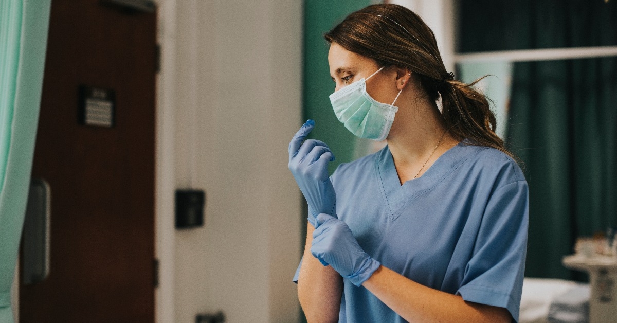 female nurse with a mask putting on gloves