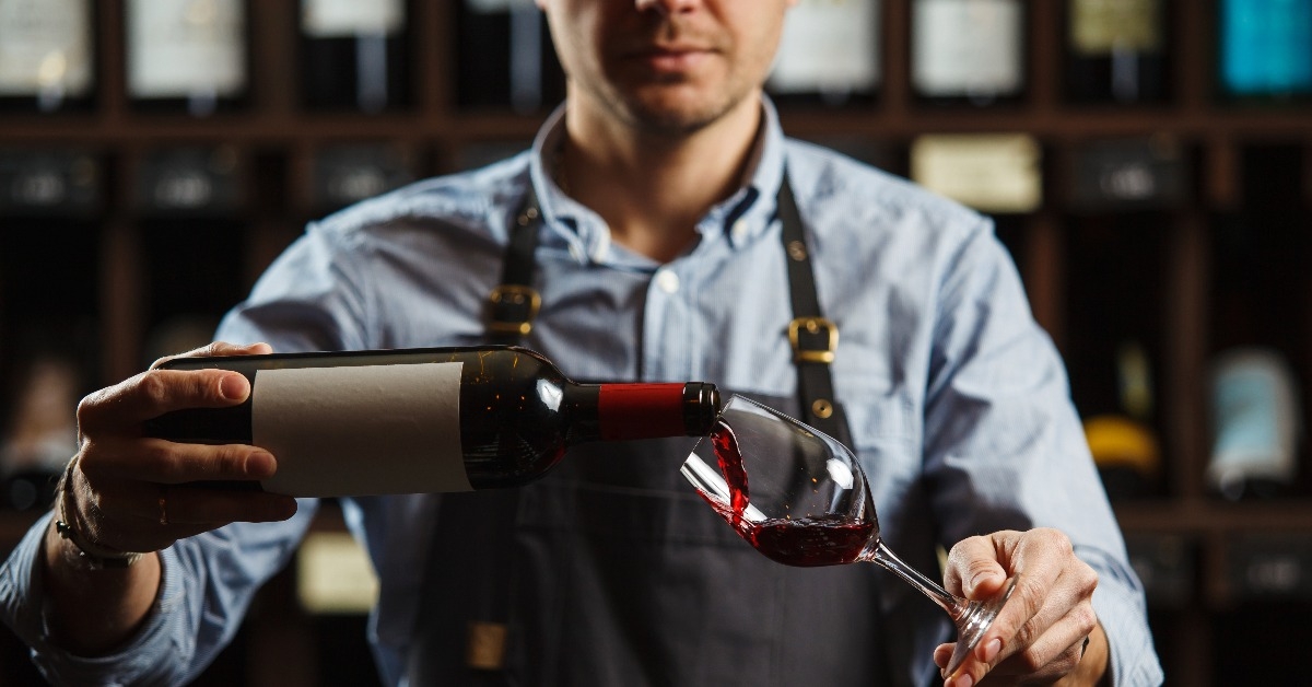male sommelier pouring red wine into long-stemmed wine glasses