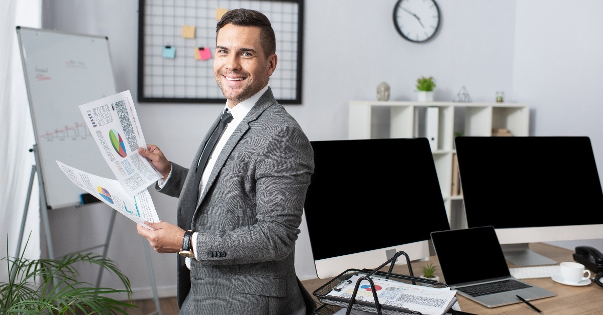 smiling trader holding infographics while standing