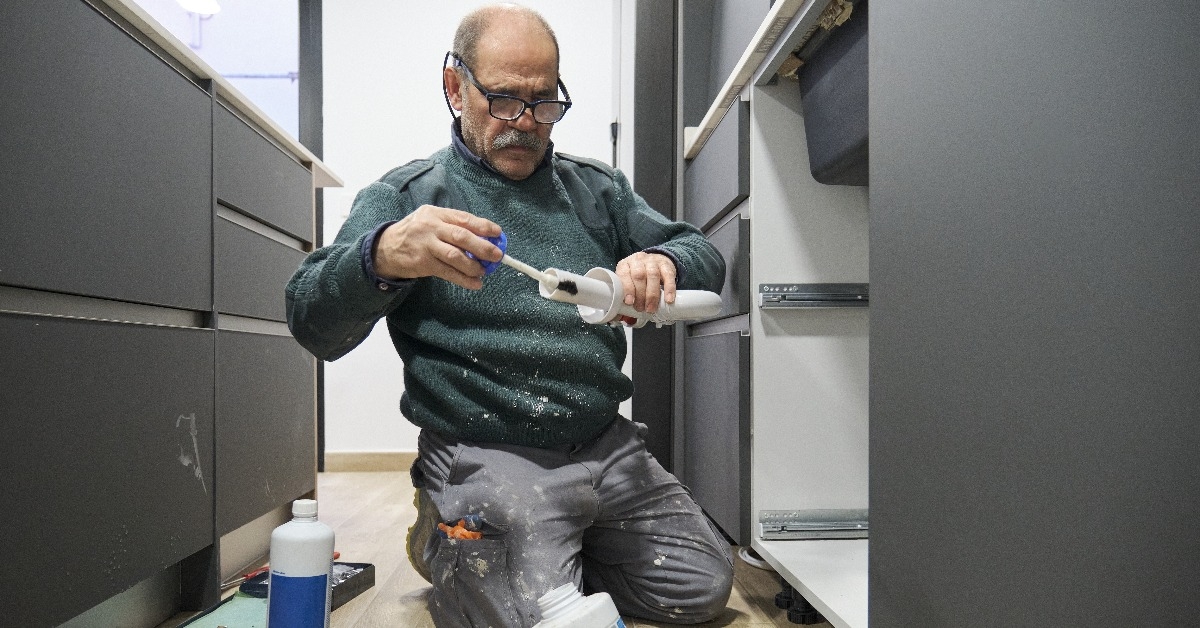 mature plumber applying glue to a sink siphon white plastic pipe