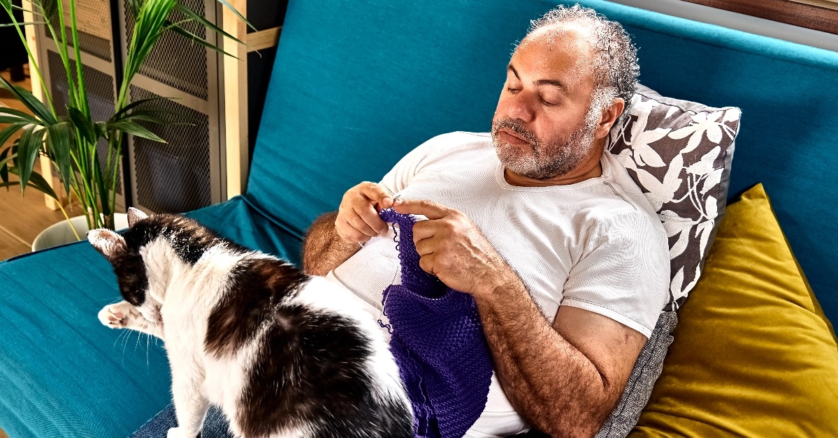 middle aged man sitting on sofa knits a violet wool scarf
