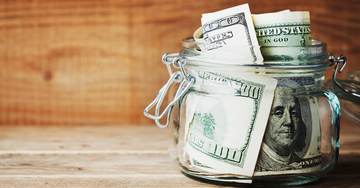 dollar bills in glass jar on wooden background