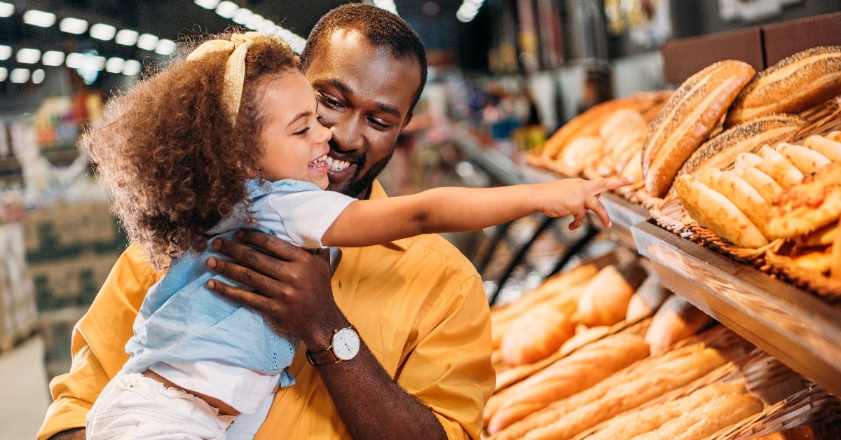 little child pointing by finger at pastry to father in supermarket
