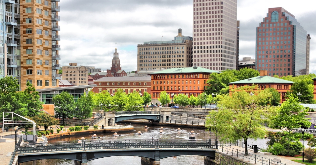 small bridge in the middle of a river with beautiful green trees and tall buildings in Rhode Island