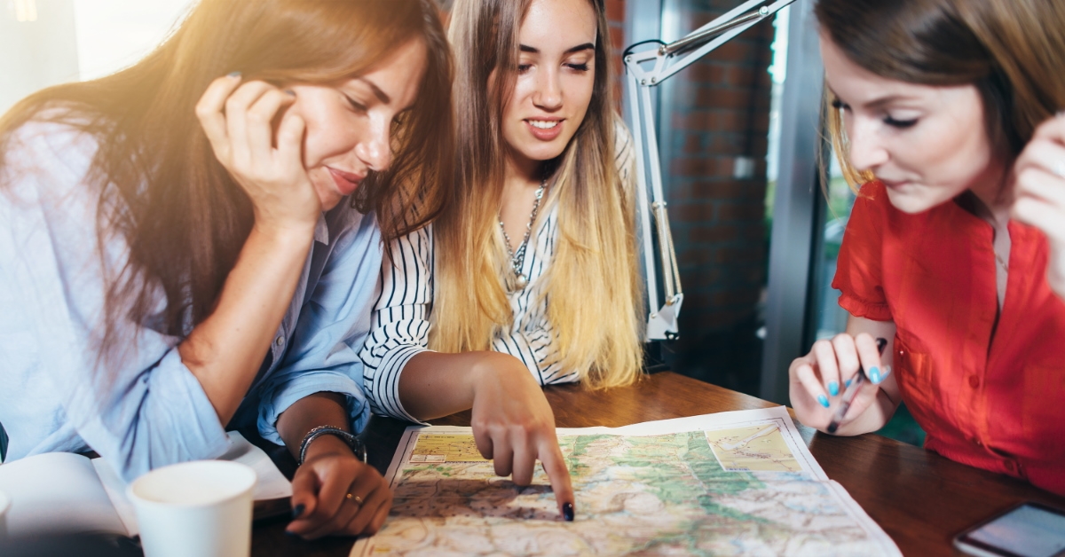 girls sitting together and checking out paper map on table