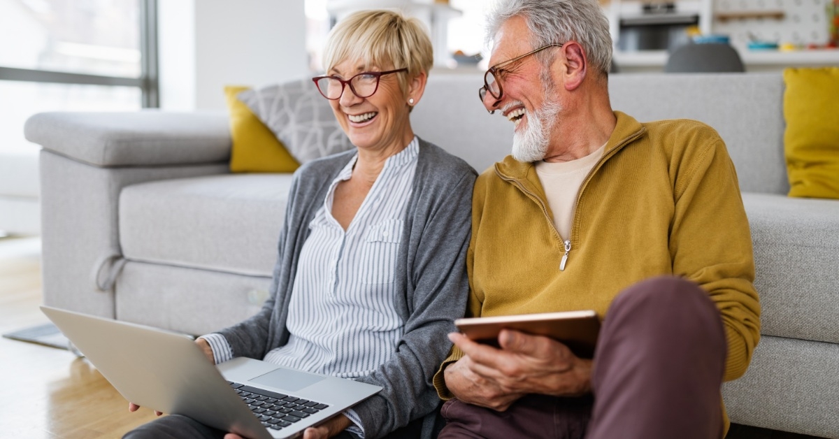 senior couple laughing using laptop and tablet at home