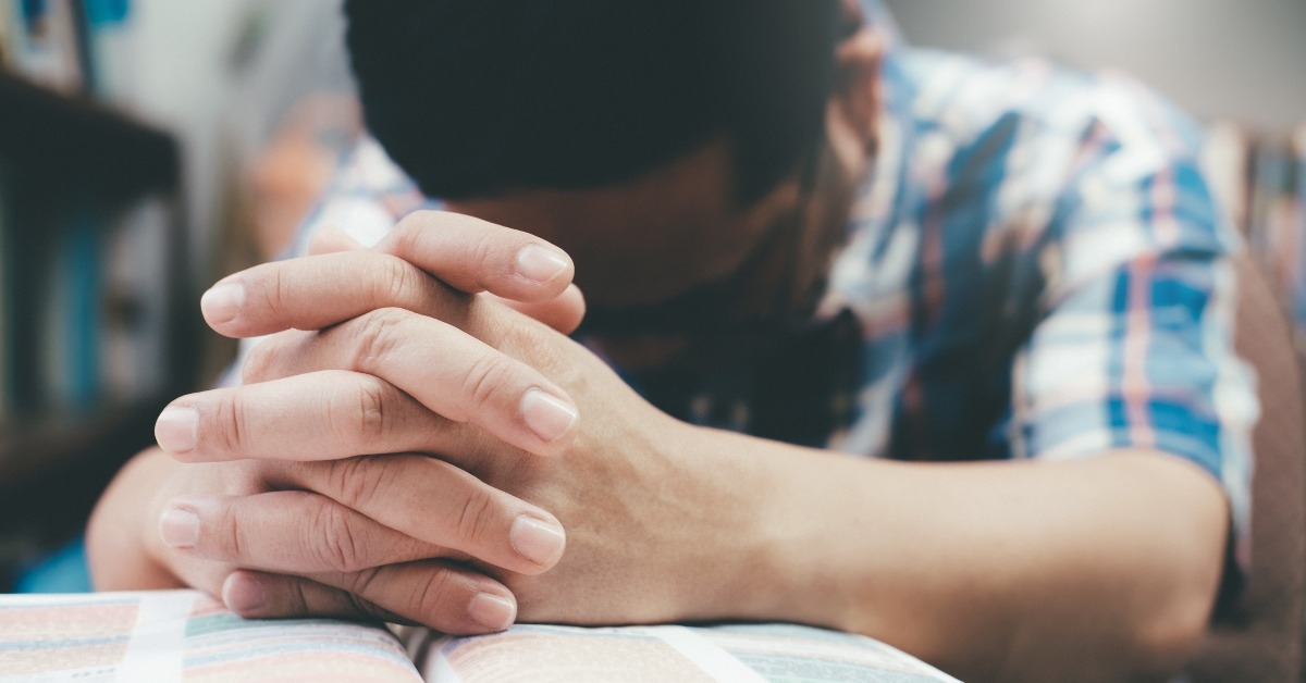 man praying with hands over the Bible
