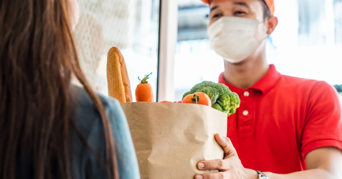 young delivery boy handing groceries in a brown bag to a lady 