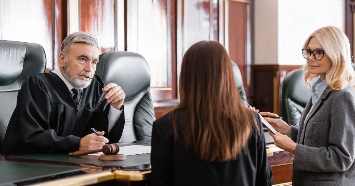 judge holding eyeglasses listens to prosecutor standing near attorney