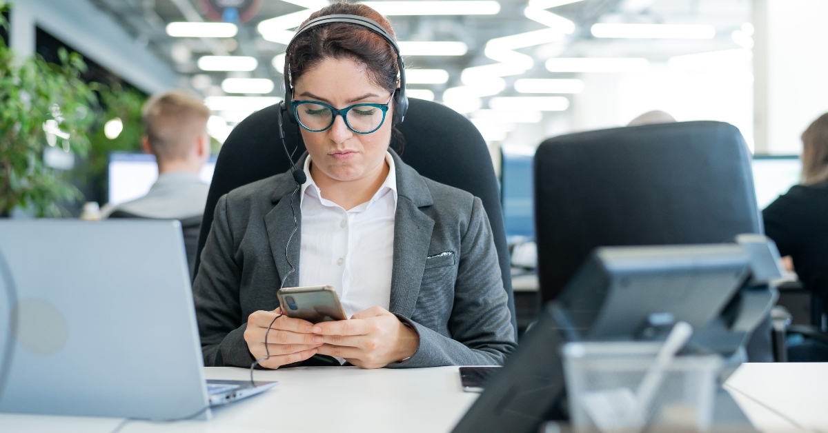 female office worker bored and uses a smartphone while sitting at a desk