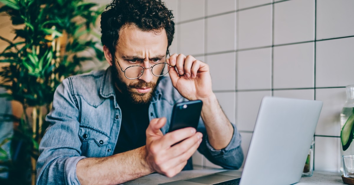 man removing glasses to read messages on mobile carefully