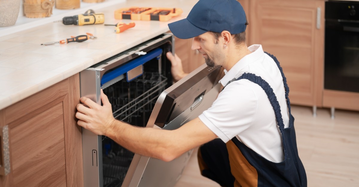 young serviceman repairing dishwasher in kitchen 