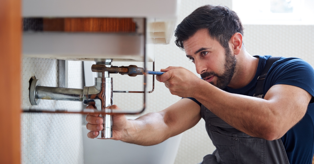 male plumber using wrench to fix leaking sink in home bathroom