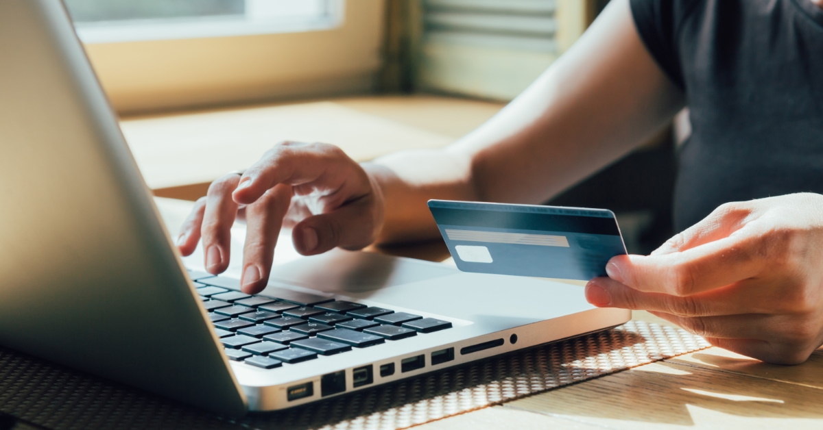 man typing on laptop while holding credit card