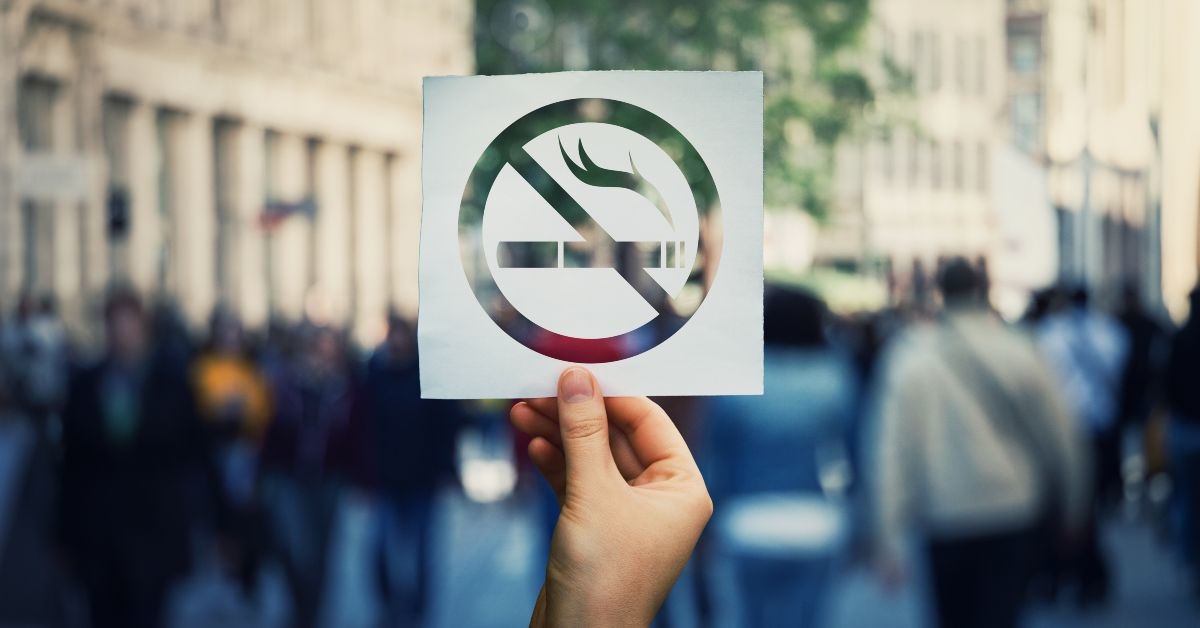 Hand holding a no smoking sign with blurred crowd in the back