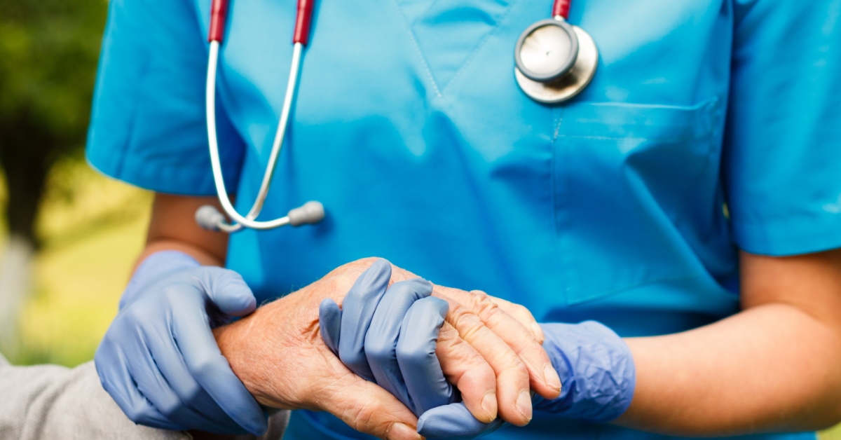 doctor in blue scrubs wearing stethoscope holding hand of senior person