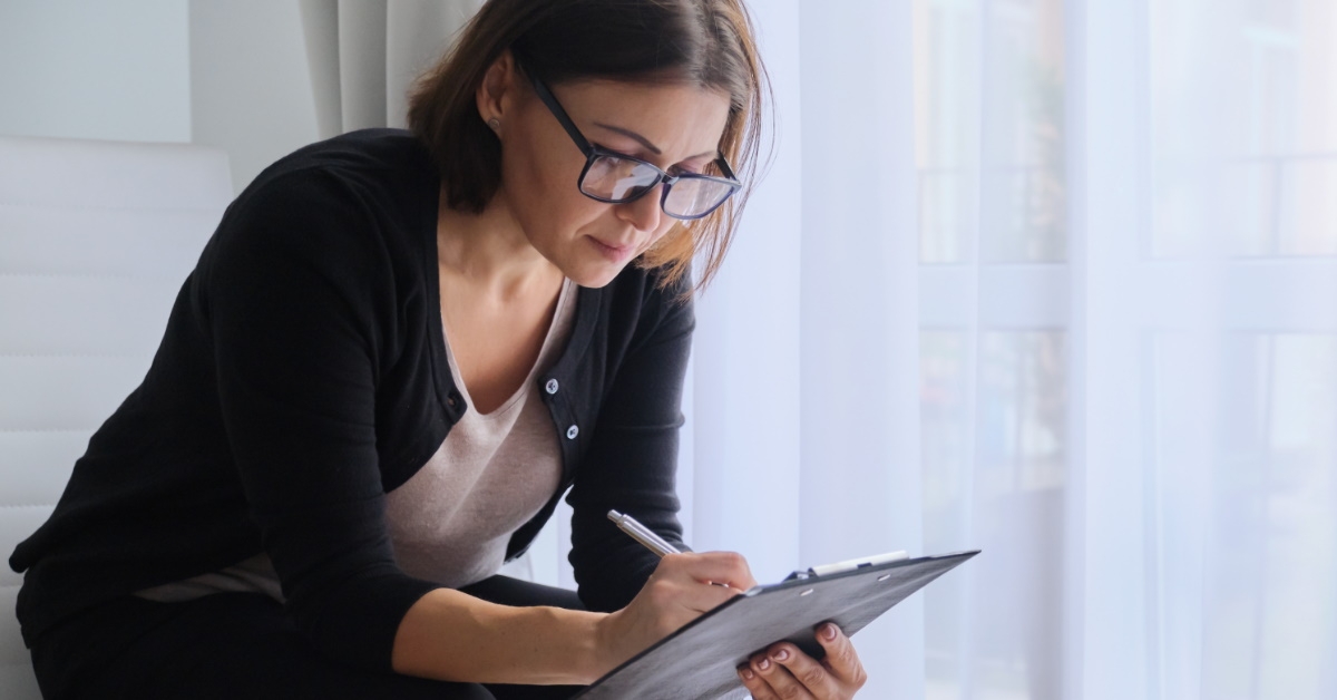 woman wearing glasses writing on notepad with pen