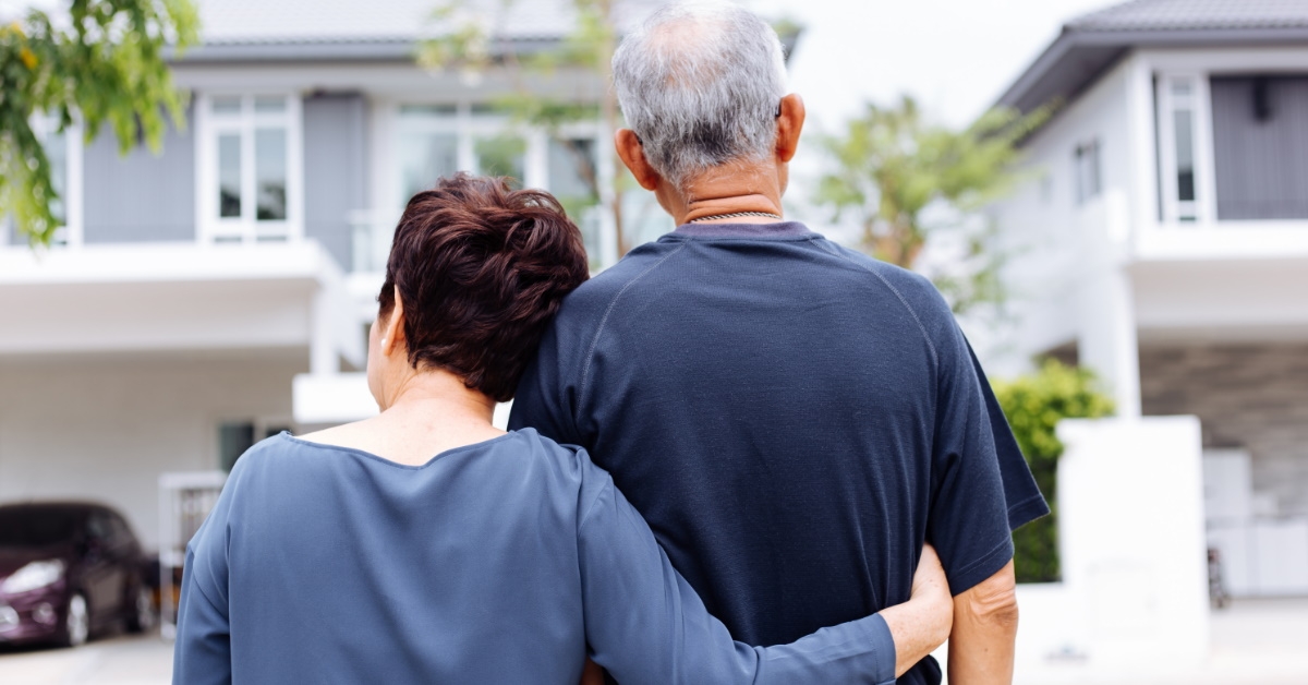 back shot of senior couple standing in front of porch of house