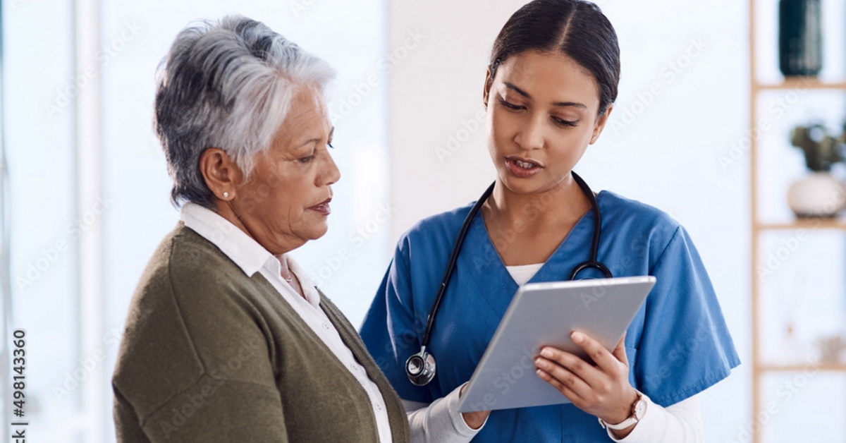 nurse wearing blue scrubs explaining to senior lady on tablet