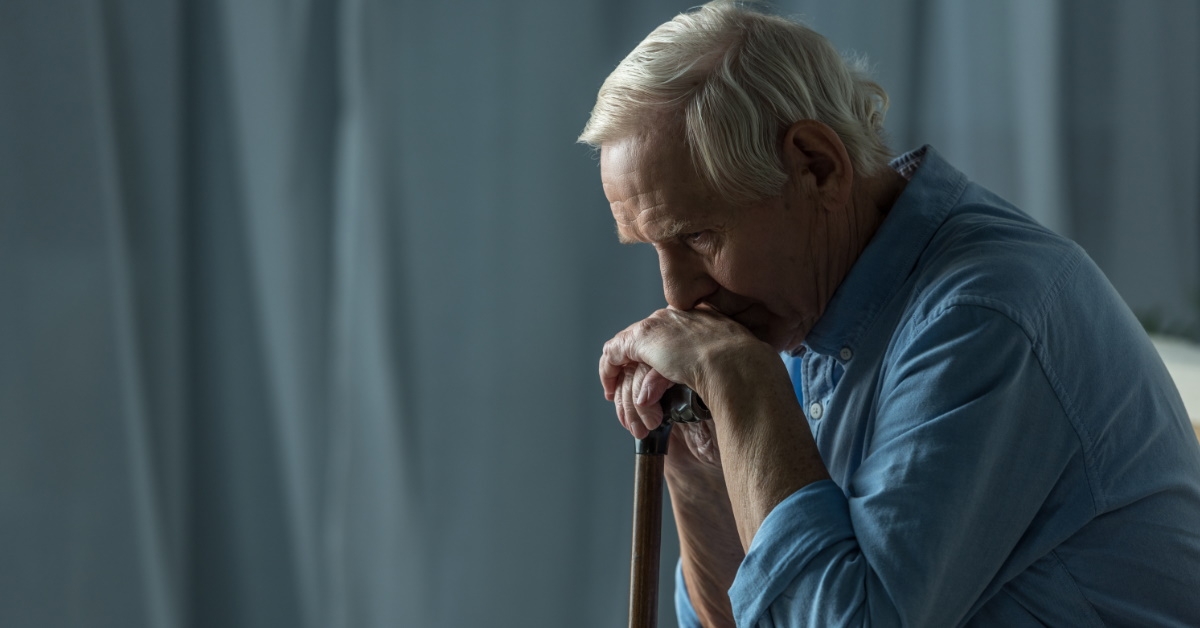 sad senior man leaning on cane in room